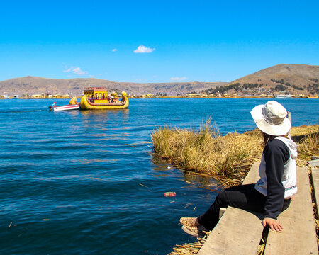 mulher no lago Titicaca, Bol&iacute;via, com barco de totora ao fundo 