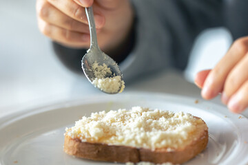 A woman sprinkles a piece of bread with grated cheese.