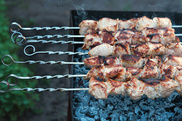 Lots of metal skewers with meat cooking on coals. Cooking pork barbecue.