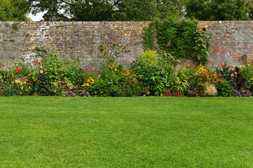 Scenic view of a grass lawn, flowers in bloom and an old wall in a beautiful garden