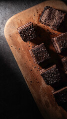A chocolate sponge cake drizzled with chocolate sauce is served on a wooden cutting board, isolated against a kitchen background.