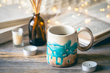 Cozy composition with a cup on a blurred background with books and bokeh lights.