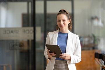 Smart businesswoman stands using digital tablet in office.