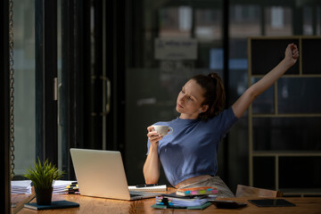 Businesswoman stretching lazy at the desk to relax while take a break from work and enjoy with coffee in the office. Feeling stressed and achy from work.