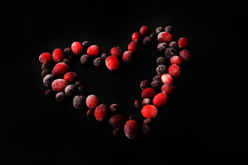 frozen cranberries and black currants on a black background in the shape of a heart