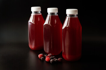 three plastic bottles with cranberry and currant juice and frozen berries on a black background