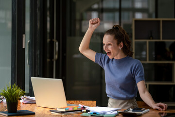 Fototapeta premium Happy business woman celebrating victory while receiving good news on her laptop, excited about success.