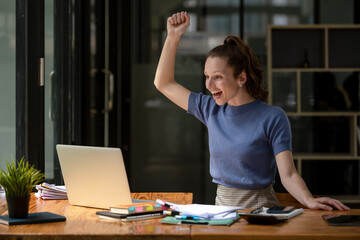 Happy business woman celebrating victory while receiving good news on her laptop, excited about success.