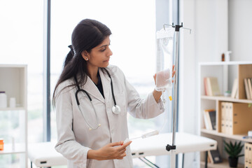 Adult female doctor in white lab coat standing near medical dropper and controlling liquid...