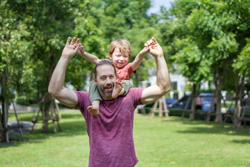 Obraz premium A happy father is playfully lifting his young son high, in a bright, green park.