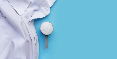 Detergent powder in measuring spoon with cloth before washing. Laundry concept.