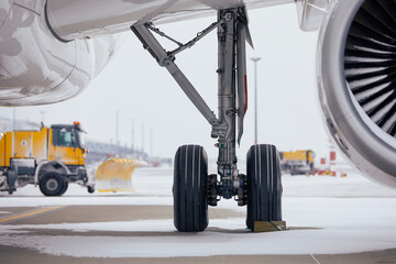 Winter day at airport during snowfall. Selective focus on snowy airplane. Snowplows clearing snow from runway..