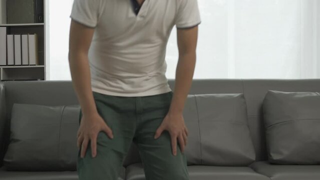 A young man with hemorrhoids cannot sit. Unhealthy man feeling sick, hemorrhoids pain, sitting on the sofa, suffering pain