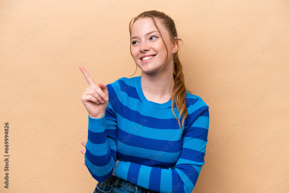 Sticker Young caucasian woman isolated on beige background pointing up a great idea