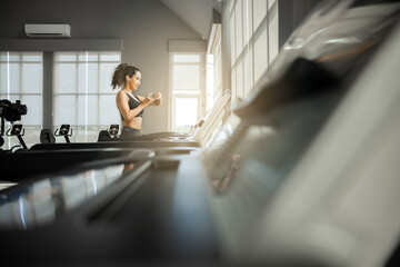 Athletic woman before start running setting up her smart watch while standing on the treadmill in...