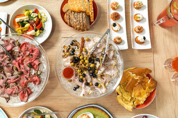 Scene of a table with appetizers. Top view on white wooden background. Board with appetizers, meat with capers, cheese, assorted holiday dishes. Olives, Italian bread.