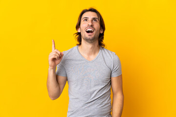 Young handsome man isolated on yellow background pointing up and surprised