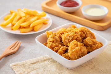 Crispy popcorn chicken in bowl with french fries on plate and sauce.
