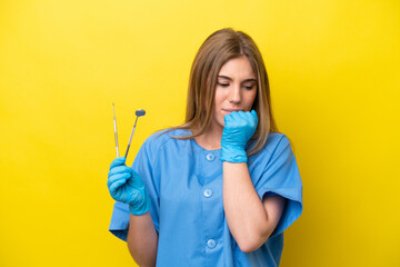 Dentist caucasian woman holding tools isolated on yellow background having doubts