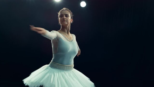 Cinematic Performance of a Talented Ballerina Dancing on a Dark Stage with Lights. Young Female Moving in a Beautiful Dress, Making Ballet Pirouettes and Spinning and Jumping on Her Toes
