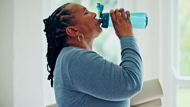 Senior woman, drinking water and bottle with yoga mat for hydration, energy and wellness in home. Elderly African lady, training and exercise for health with detox, nutrition and diet in house