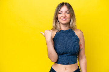 Young Rumanian woman isolated on yellow background pointing to the side to present a product