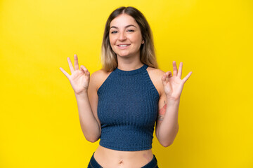 Young Rumanian woman isolated on yellow background showing ok sign with two hands