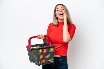 Young Rumanian woman holding a shopping basket full of food isolated on white background shouting with mouth wide open
