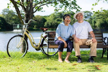 Happy and healthy couple Asian sitting chair beside a bicycle Family and friendship lifestyle, Enjoyment of active seniors, and outdoor activity after retirement, health care insurance concept