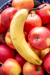 Banana and ripe red apples in a bowl in the kitchen.