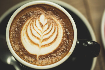 Closeup white cup of hot coffee latte on wood background in restaurant.Leaf tree texture coffee latte art make by barista on best of menu in the coffee shop.Soft focus