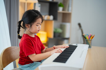 Happy little asian cute baby girl smile playing learning online piano music in living room at home....