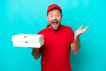 Pizza delivery man with work uniform picking up pizza boxes isolated on blue background with shocked facial expression