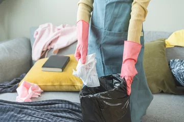 Fotobehang Tired household clean up, housekeeper asian young woman, girl hand holding tissue, napkin paper put in trash bin, cleaning in living room at home. Messy maid or housewife organizing dirty and untidy. © KMPZZZ