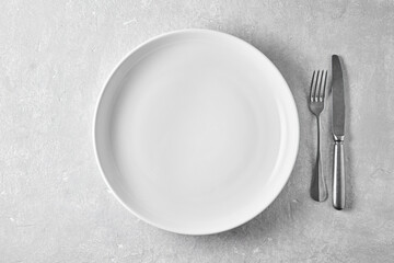 Empty white plate and fork with knife on a gray concrete table. Top view with copy space