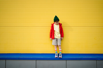 Boy wearing red jacket standing in front of yellow wall