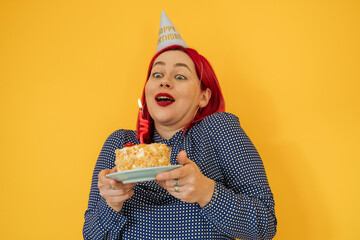 Surprised woman holding birthday cake against yellow background