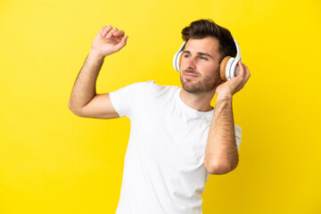 Young caucasian handsome man isolated on yellow background listening music and dancing