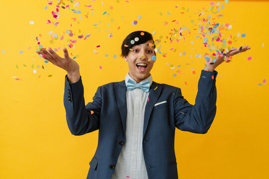 Joyful man throwing confetti and enjoying against yellow background
