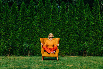 Blond woman sitting and meditating on chair in garden