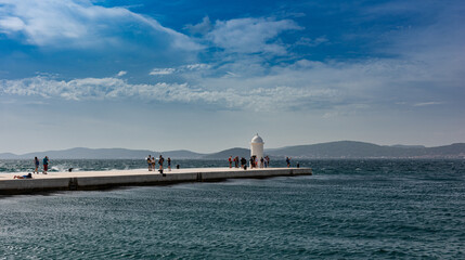 Small white lighthouse and people on pier. Seascape view from Zadar, Croatia.