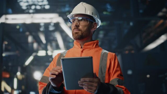 Serious factory supervisor looking at manufacturing making notes tablet close up