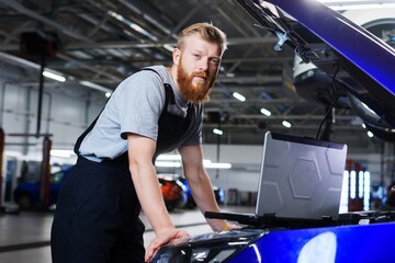 Portrait of a professional automotive electrician who diagnoses car errors using a laptop against the background of a service station