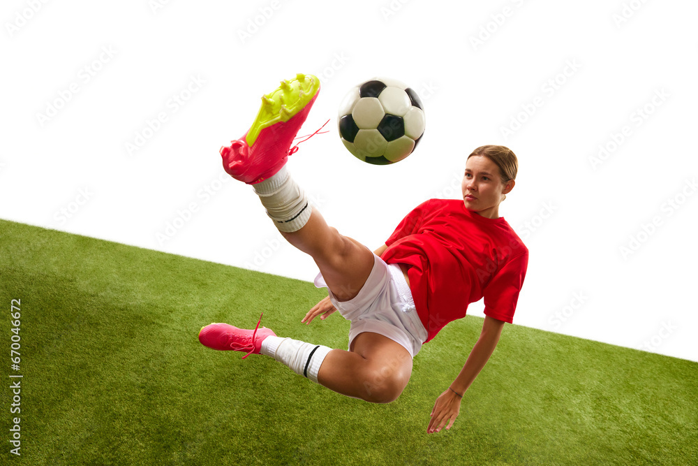 Wall mural Concentrated female football player in motion, hitting ball and falling down during game in grass field isolated on white background. Concept of sport, competition, action, success. Copy space for ad