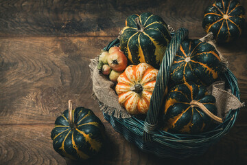 Basket with various small pumpkins on wooden background, a female hand taking one pumpkin