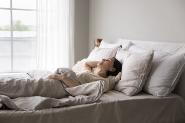 Older woman sleeping alone in double bed in modern, light bedroom, looks serene while resting in...