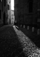 silhouettes of a girl tourist observing the ancient buildings in the ancient village of upper Bergamo - street photography in black and white. - 670049480