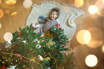 Little toddler boy is lying under decorated Christmas tree at home, view from above. Smiling child during Winter Holidays. . High quality photo
