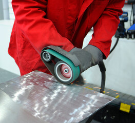 Worker hands sanding metal sheet by the hand held belt sender