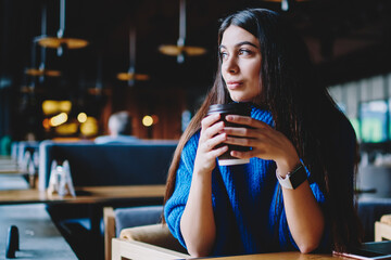 Thoughtful hipster girl looking aside while sitting at cafe and drinking coffee
